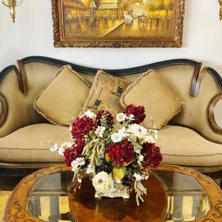 A cozy living room setup featuring an elegant sofa, a floral centerpiece on a coffee table, and a framed painting on the wall.