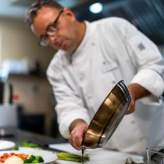 A professional chef skillfully pouring sauce in the kitchen.