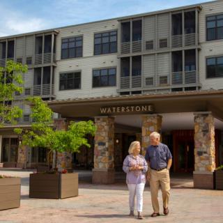 An elderly couple walking in front of a modern building on a sunny day.