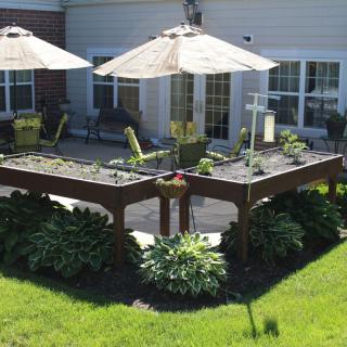 A beautifully landscaped garden featuring raised beds and outdoor seating with umbrellas.