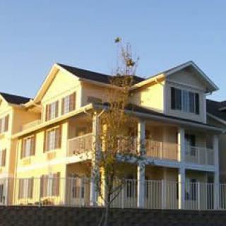 A two-story residential apartment complex with a yellow exterior, bathed in daylight.