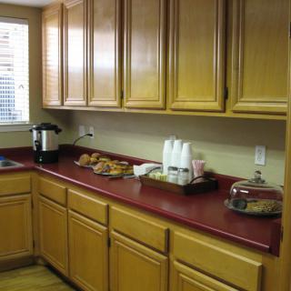A kitchen with wooden cabinets and a red countertop, featuring snacks, a coffee maker, and baked goods.