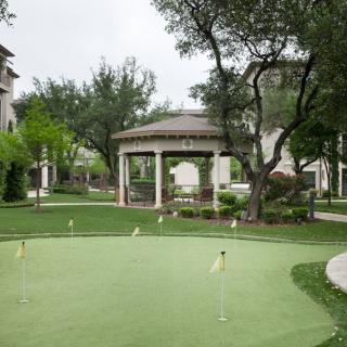 A serene outdoor setting featuring a gazebo and a well-maintained putting green, surrounded by lush greenery and trees.