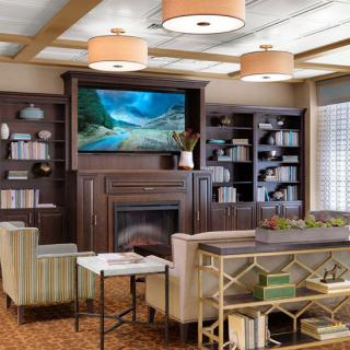 A cozy living room with modern decor featuring a television above the fireplace, bookshelves, and comfortable seating.