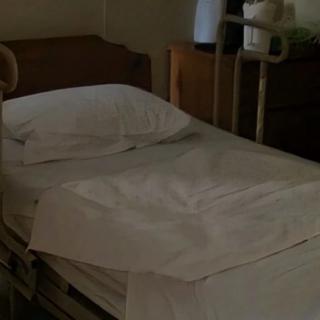 An empty hospital bed with neatly arranged white sheets in a medical setting.
