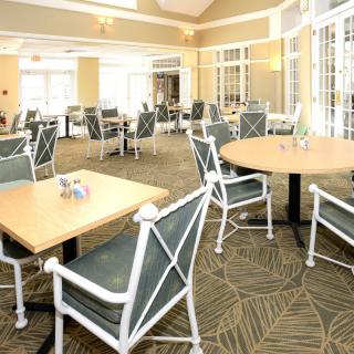A well-lit dining area with neatly arranged tables and chairs on a carpeted floor.