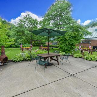 A peaceful garden patio with a table, chairs, and an umbrella surrounded by lush greenery.