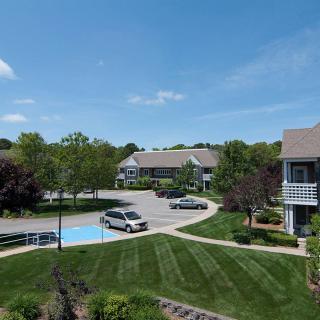 A view of a well-maintained residential apartment complex with lush landscaping, parked cars, and clear blue skies.