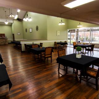 A spacious dining area with wooden floors and neatly arranged tables and chairs.