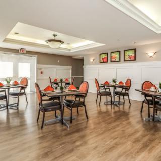 A well-lit dining area with neatly arranged tables and chairs, featuring elegant decor and a wooden floor.