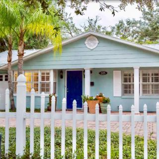 Charming blue cottage with a white picket fence and lush greenery.