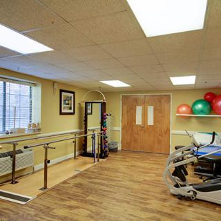 A well-equipped physical therapy room with parallel bars, a stationary bike, and exercise balls.