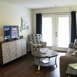 A cozy living room setup with a TV, stylish armchairs, and a sofa, complemented by dark curtains and a hardwood floor.