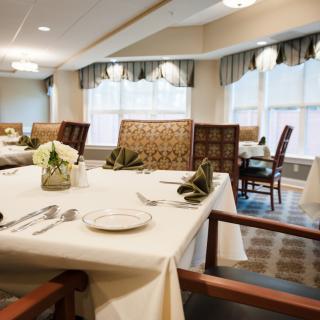 An elegant dining room with tables neatly set, featuring white tablecloths, folded napkins, and stylish decor.