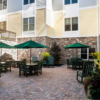 A well-furnished outdoor patio area with tables, chairs, and umbrellas in front of a building.