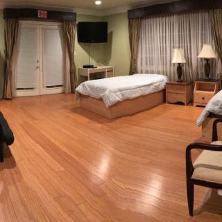 A spacious bedroom interior with wooden flooring, featuring a single bed, bedside tables with lamps, a television, and elegant curtains.