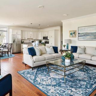 A stylish open-concept living room with a blue-themed decor, featuring comfortable sofas and a modern kitchen in the background.