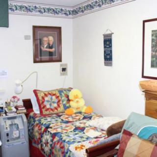 A cozy bedroom setup with a colorful quilt and a stuffed duck on the bed, adorned with various wall decorations.