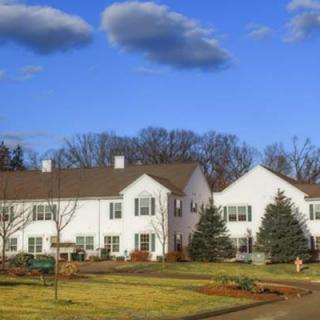 A view of a residential building with white exteriors and surrounding greenery under a blue sky.