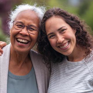 Two women smiling and embracing outdoors.