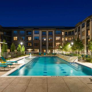 A well-lit apartment complex with a large swimming pool at night.