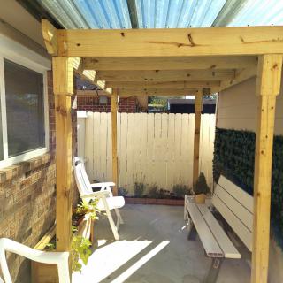 A cozy patio with a wooden pergola, featuring outdoor seating including a bench and chairs.