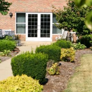 A well-maintained garden with shrubs lining a walkway leading to a brick building's patio doors.
