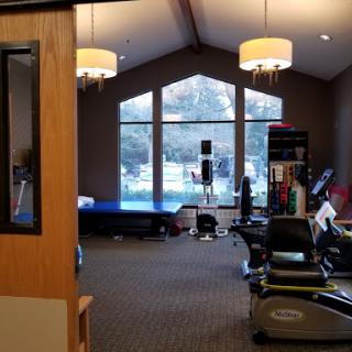 A view of a fitness center featuring various exercise equipment and large windows allowing natural light.