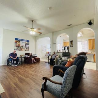 A spacious living room with a ceiling fan, hardwood floor, and various seating options, connected to an open kitchen through arched doorways.