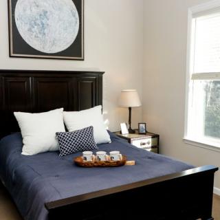A cozy bedroom with a dark bed frame, adorned with white and patterned pillows, featuring moon artwork above the headboard.