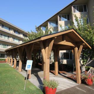 A view of a building entrance with a wooden walkway leading to an apartment complex under a clear blue sky.