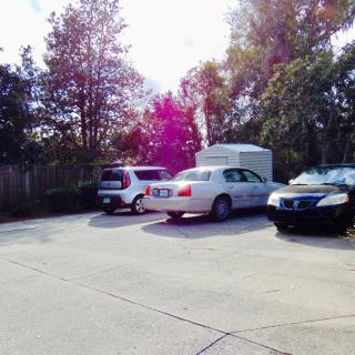 A parking lot with several cars under a clear sky surrounded by trees.