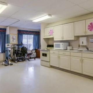 A room featuring a kitchen area with white cabinets and exercise equipment in the corner.
