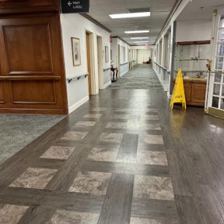 A well-lit hallway featuring wooden flooring and a caution sign, suggesting cleaning or maintenance.
