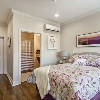 A modern bedroom with floral bed linens, artwork on the wall, and an air conditioner.