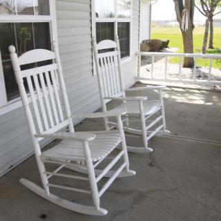 Two white rocking chairs sit on a porch, overlooking a green lawn.