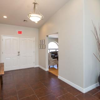 A spacious hallway with tile flooring, featuring a chandelier and an entrance door.