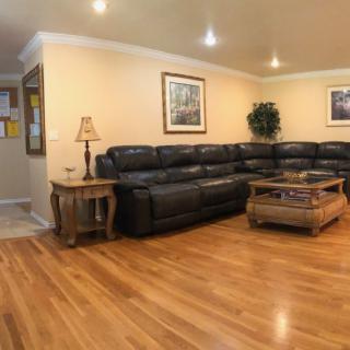 A cozy living room with hardwood flooring, featuring a large sectional sofa, a coffee table, and warm lighting.