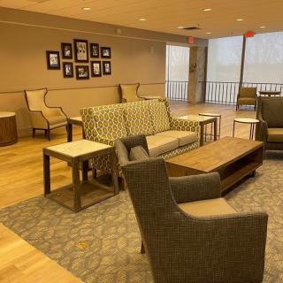 A cozy lounge area featuring various seating options with sofas, chairs, and tables, accented by wall art and a carpeted floor.