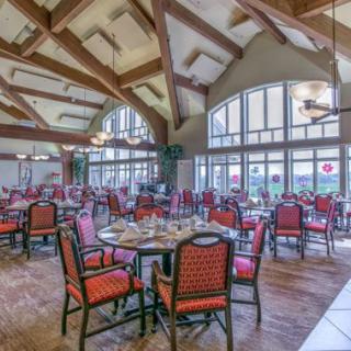 An elegant dining area with wooden beams and large windows, set up with tables and chairs.
