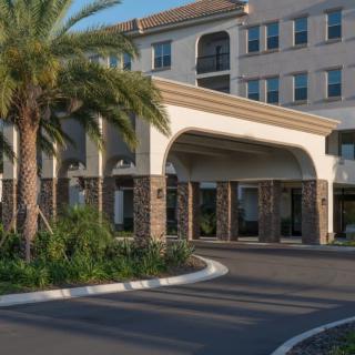 The entrance of a building with palm trees and a driveway.