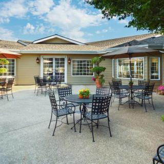 A well-furnished outdoor patio with tables, chairs, and umbrellas set against a building, ideal for relaxation under a clear sky.