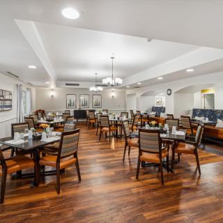A spacious dining room with neatly arranged tables and chairs on a polished hardwood floor, illuminated by elegant chandeliers.