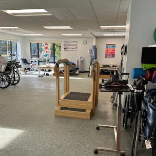 A spacious rehabilitation therapy room equipped with exercise machines and wheelchairs.