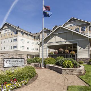 A well-maintained hotel entrance with a landscaped path and flags flying.