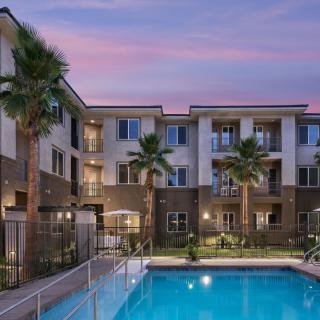 A well-lit apartment complex with a swimming pool and palm trees at dusk.