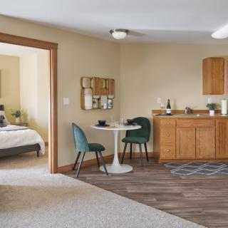 A modern and cozy apartment interior with a kitchenette, dining area, and view into the bedroom.