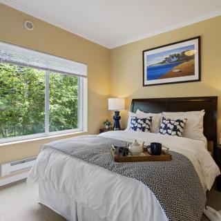 A cozy bedroom featuring a neatly made bed, large window with natural light, and tasteful decor.
