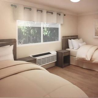 A modern bedroom with two neatly made beds, a large window with curtains, and an air conditioning unit below.