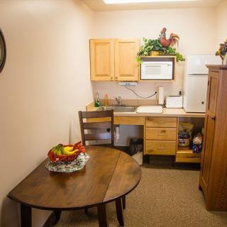 A cozy kitchenette with a round table and chairs, featuring a fruit bowl and wooden cabinets.